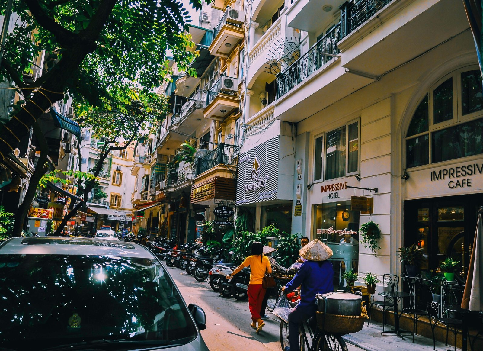 Vibrant street life in Hanoi with locals, cafes, and motorbikes on a sunny day.